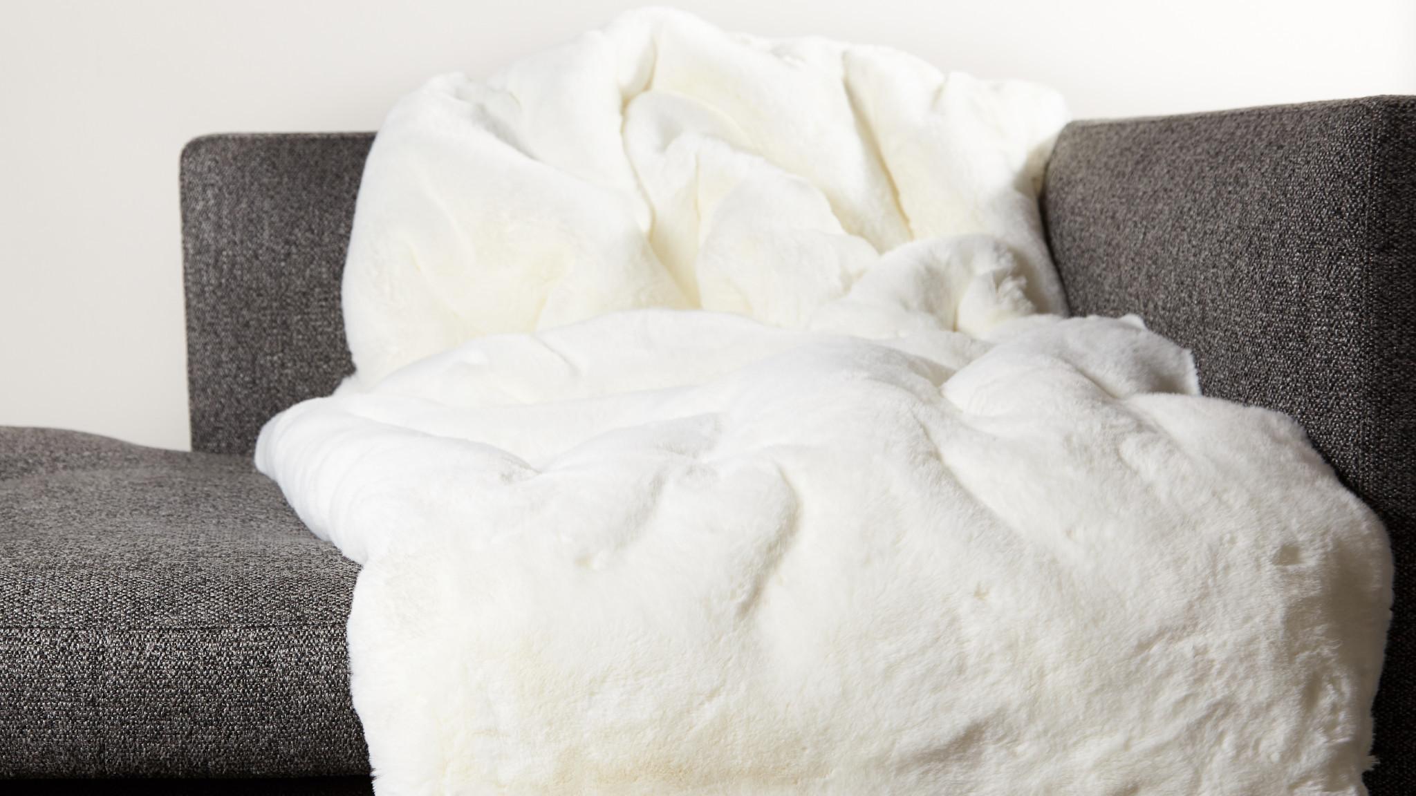 Hochflorige Webpelzdecke reinweiß sehr weich kuschlig warm auf dem Wohnzimmer Sofa mit Fütterung aus feinem weißem Wollstoff